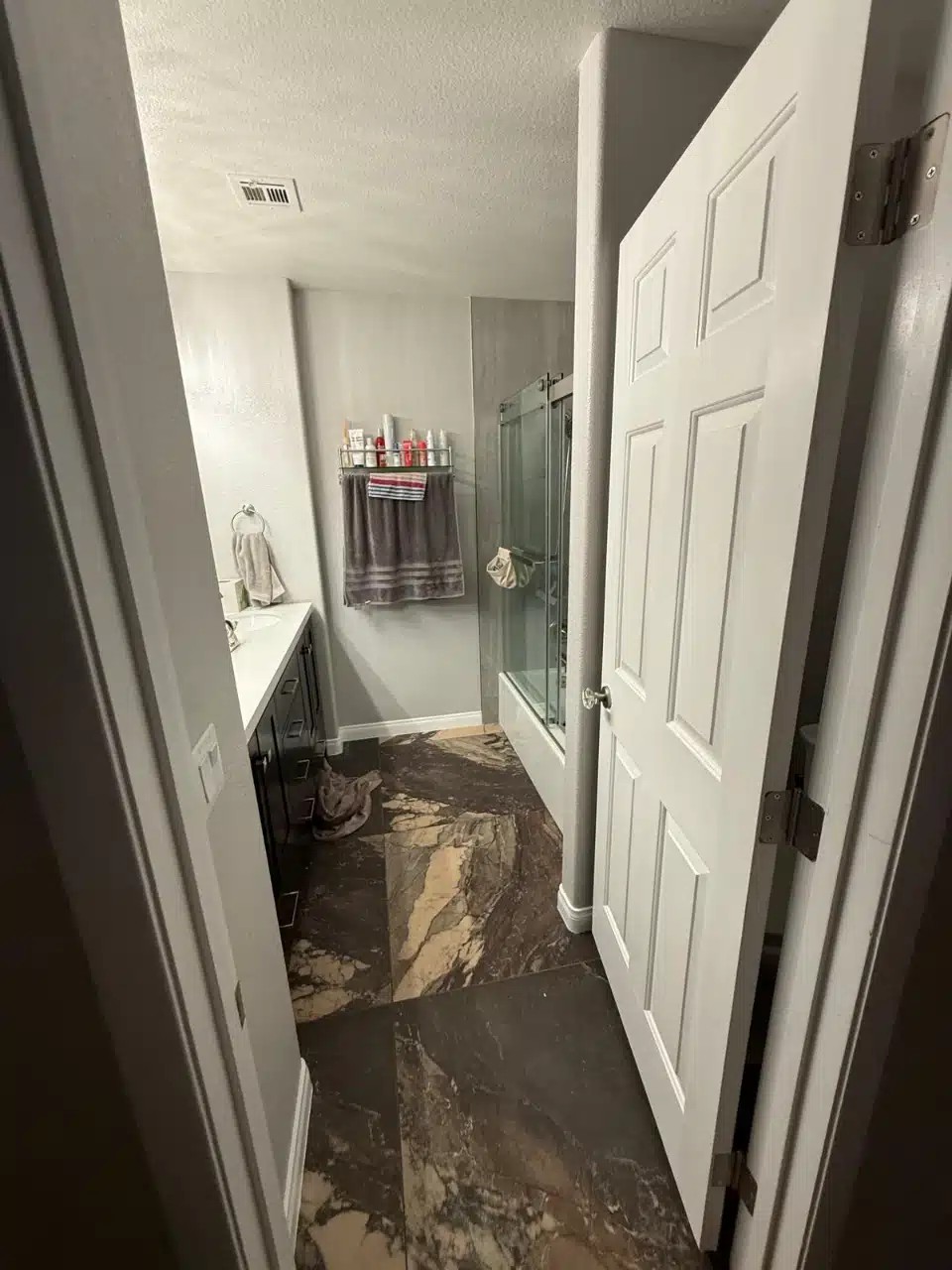 Remodeled spare bathroom with large format dark marble look porcelain floor tile running to the doorway