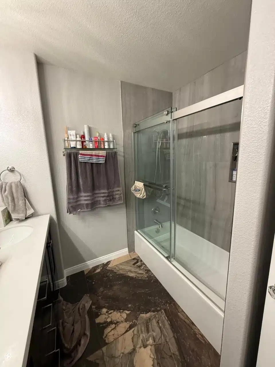 Remodeled spare bathroom tub with gray tile surround, sliding glass doors and new dark tile floor