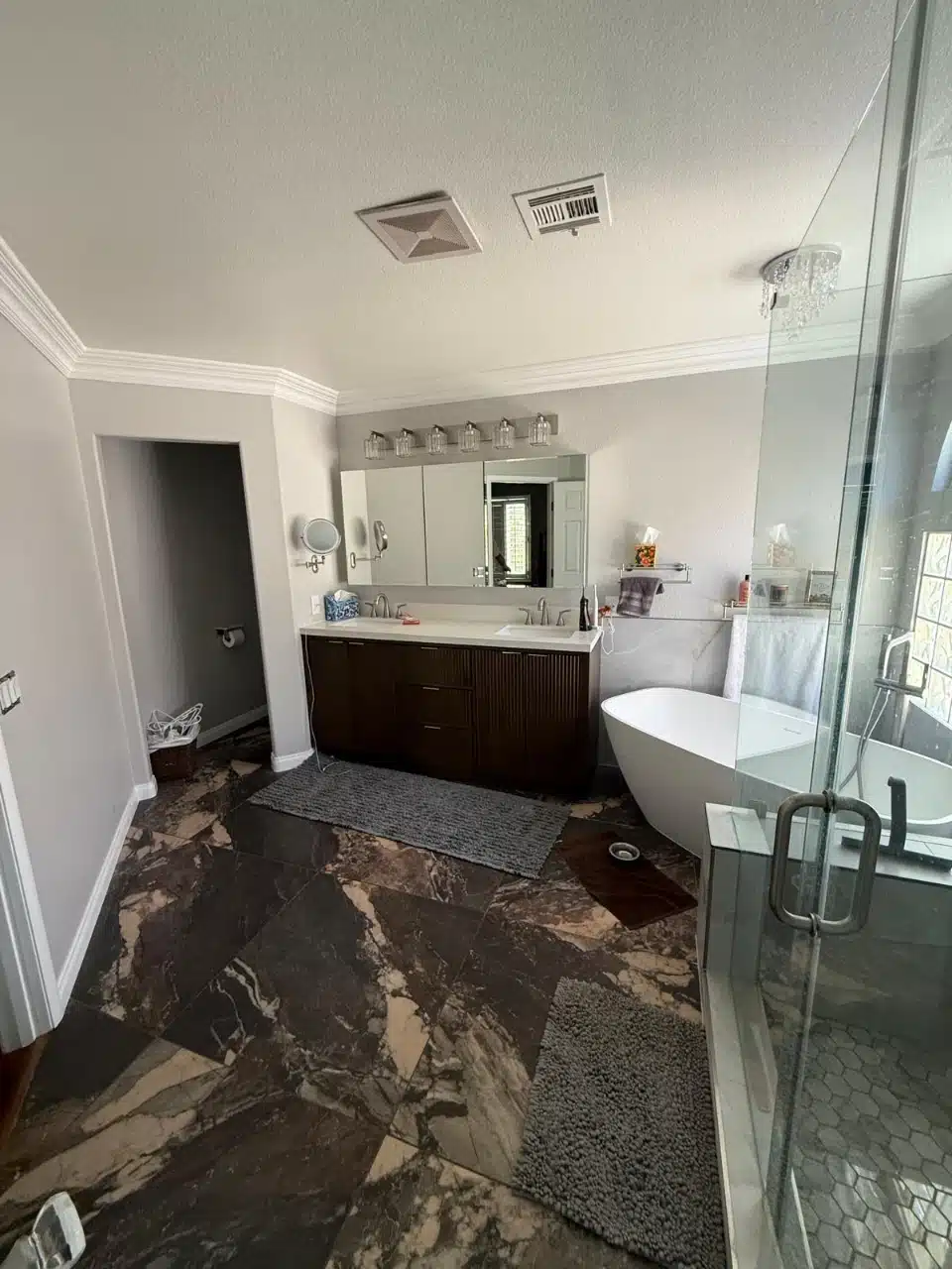 Remodeled master bathroom with freestanding white tub and dark marble look tile floor
