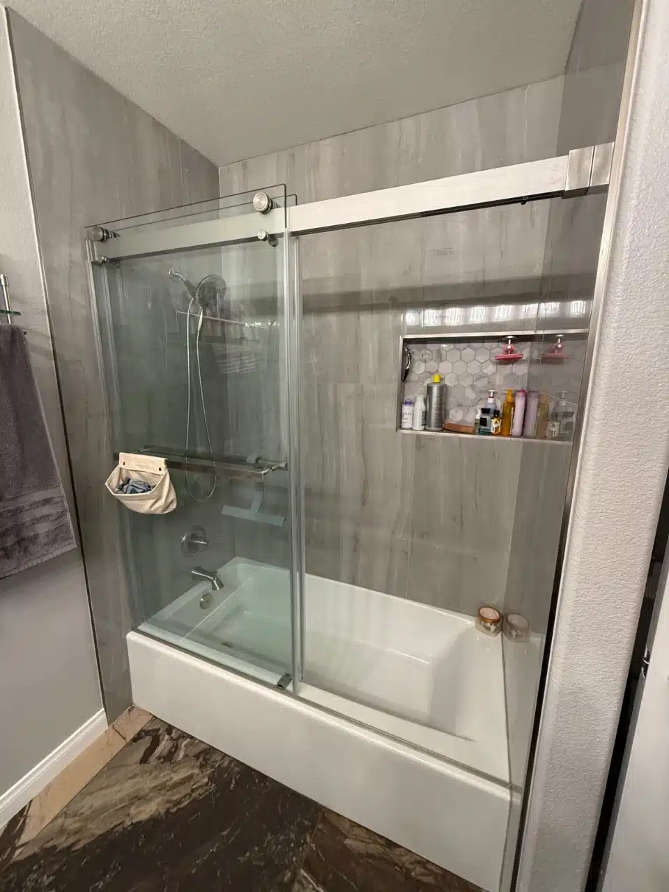 Tub shower with frameless sliding glass doors, large format gray wall tile and a recessed shower niche