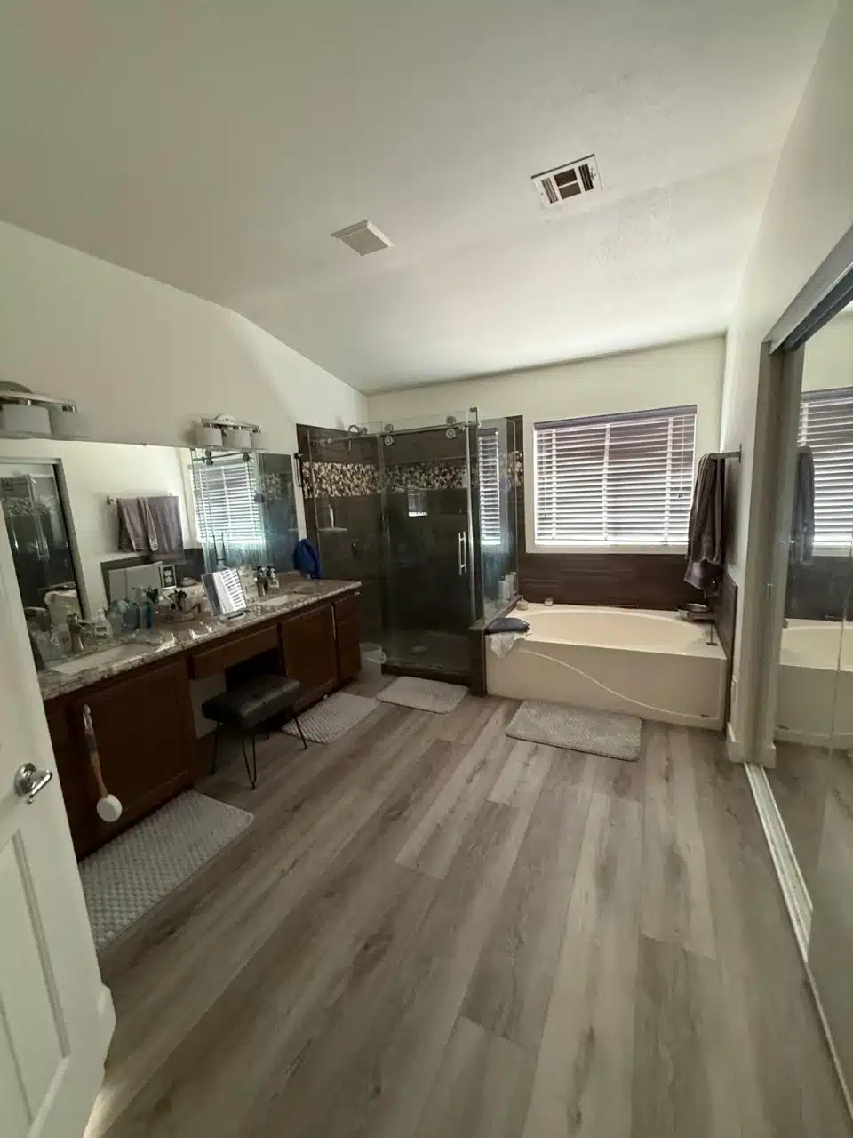 Bathroom before the remodel with dark wood vanity and makeup counter, dark tiled shower enclosure and a separate tub under the window