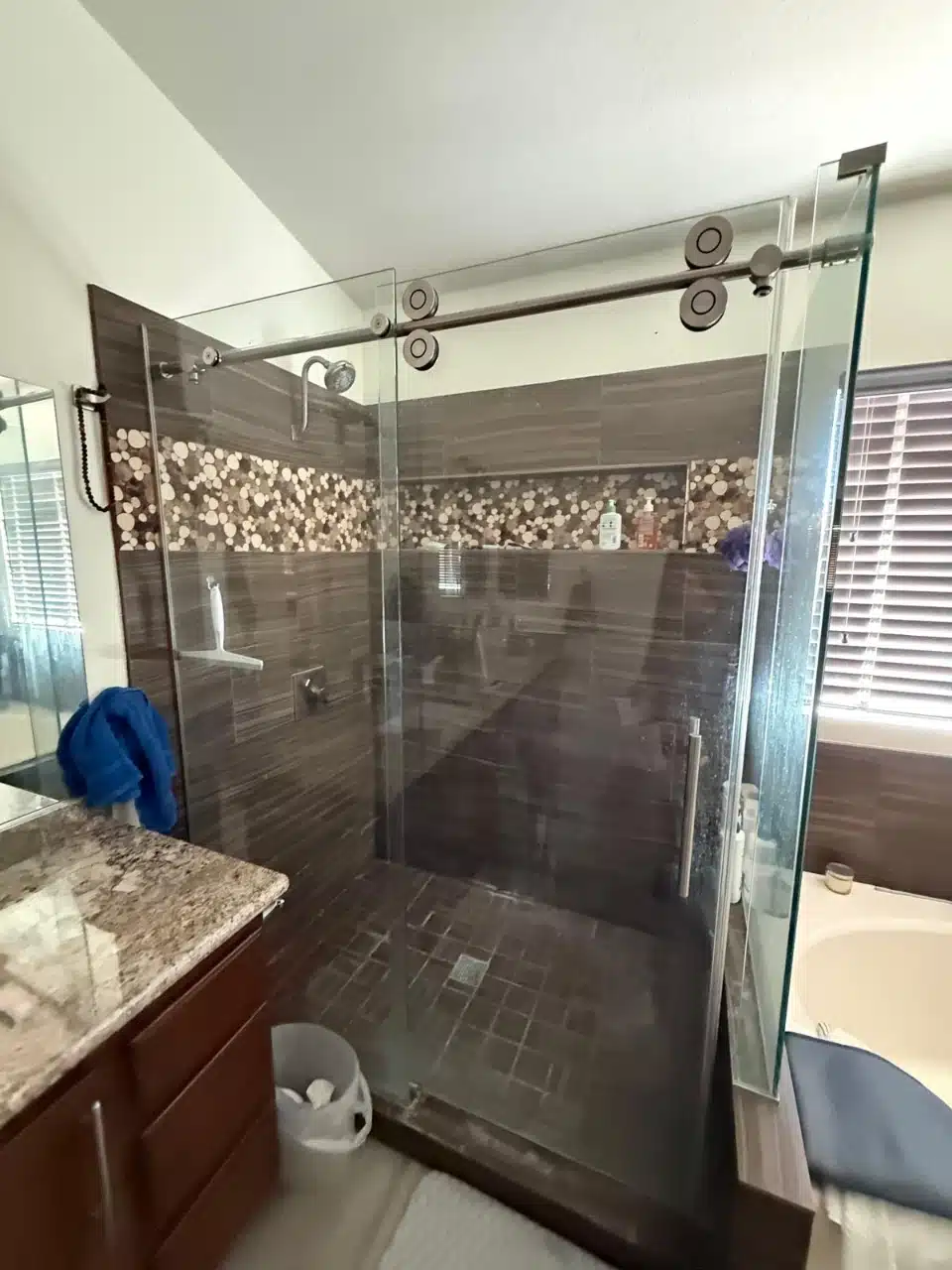 Original shower before the remodel with dark brown wall tile, a mosaic accent band and a granite vanity top