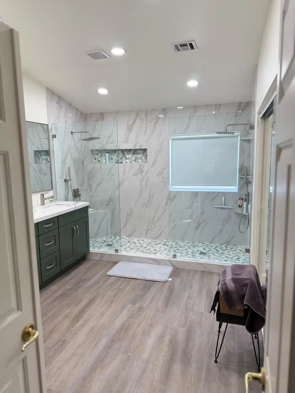 Remodeled walk-in shower with floor to ceiling marble look porcelain wall tile, pebble mosaic floor and window above