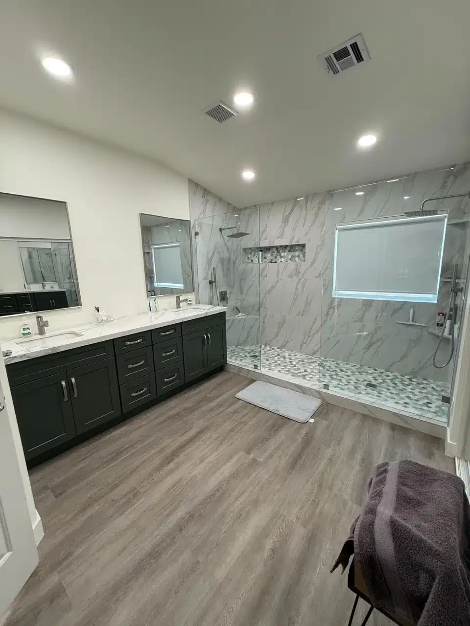 Remodeled bathroom with charcoal double vanity, recessed lighting and marble look walk-in shower
