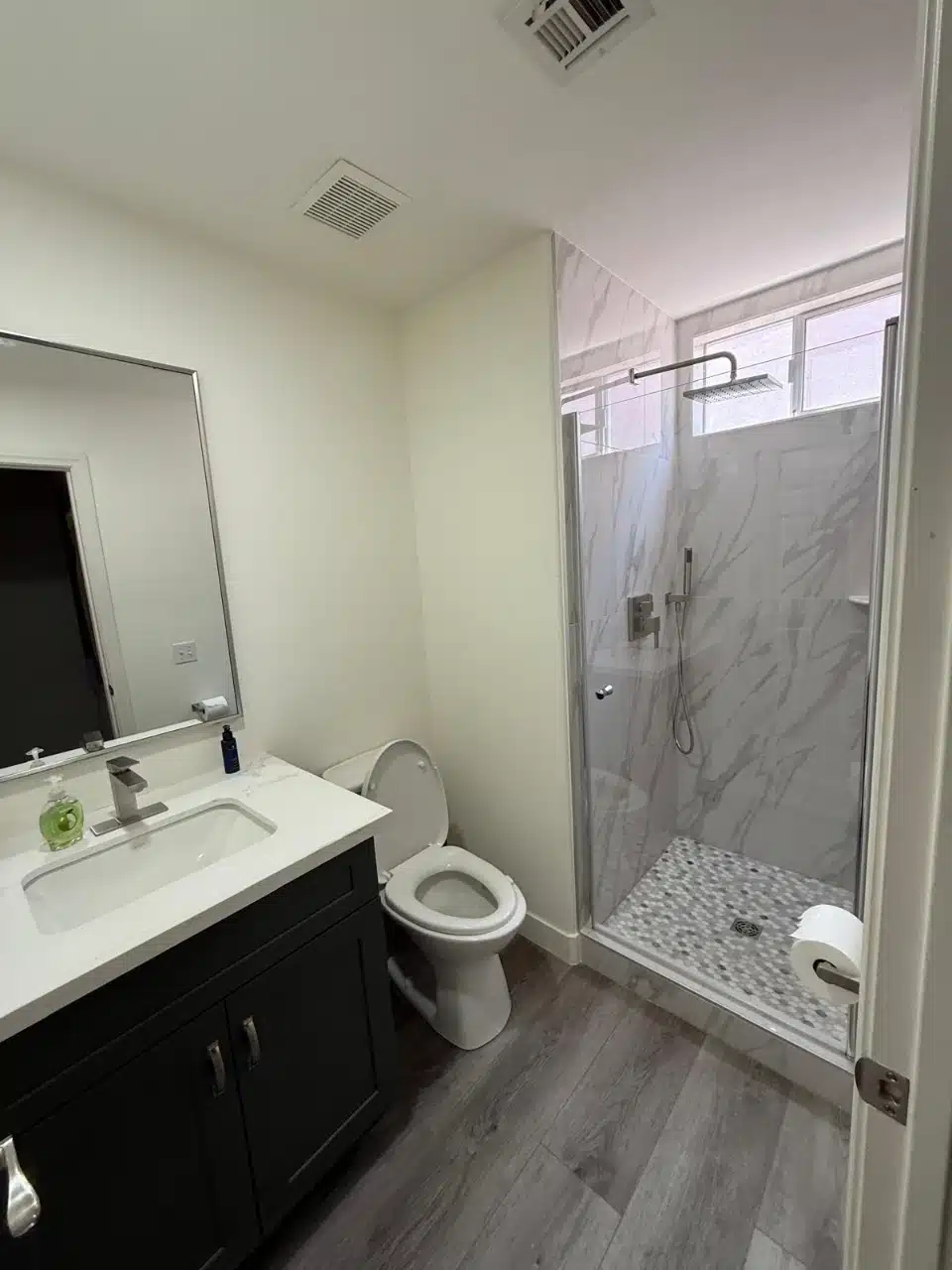 Second remodeled bathroom with charcoal vanity, white countertop, large mirror and a glass enclosed tiled shower