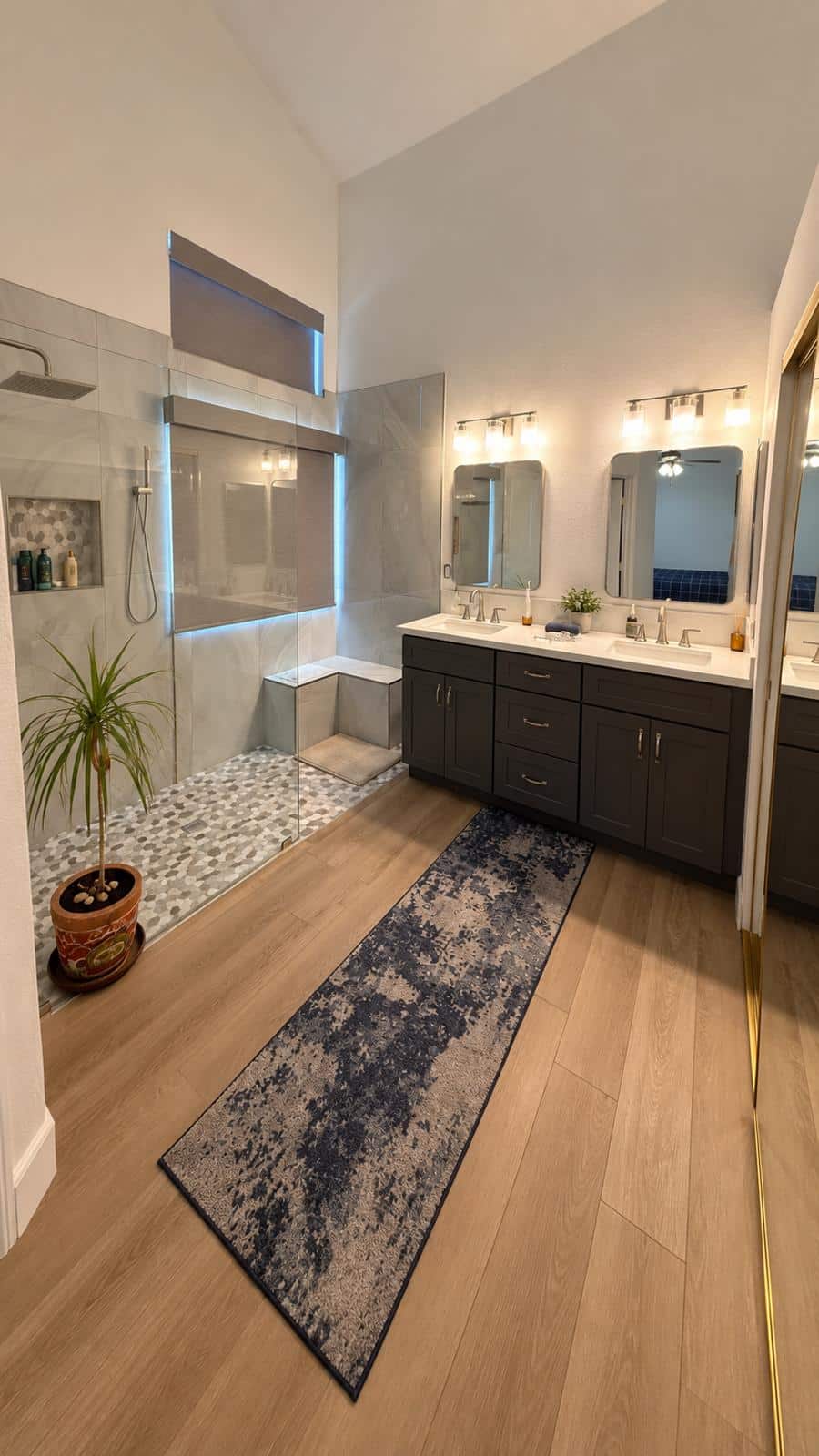 Remodeled bathroom with charcoal vanity, new light fixtures, oak vinyl plank floor and walk-in shower