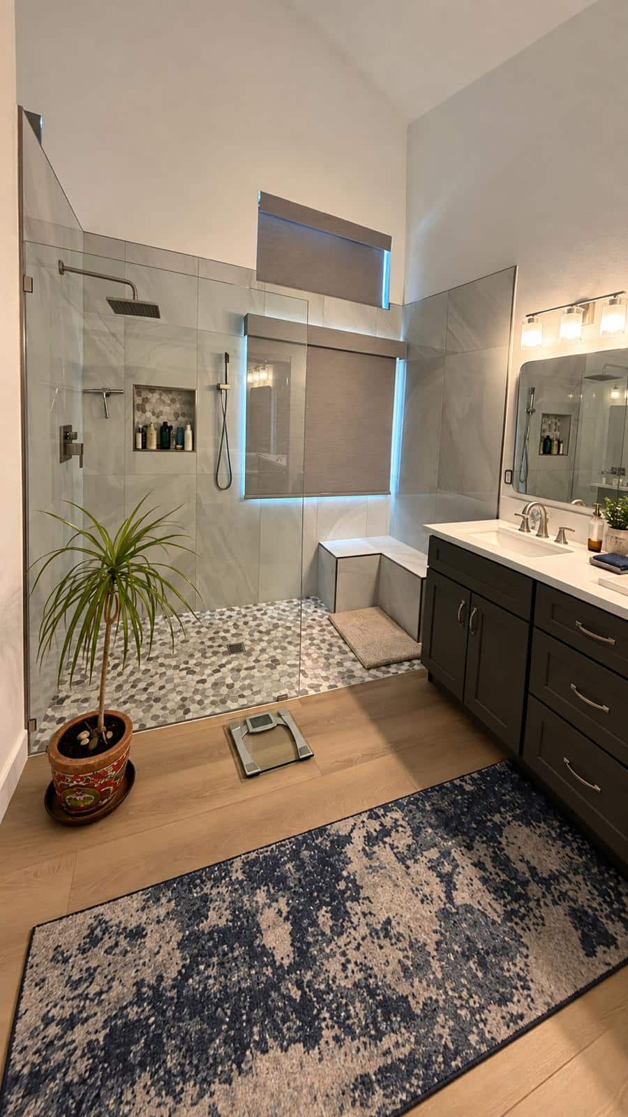 Remodeled walk-in shower with large gray tile walls, pebble mosaic floor, recessed niche and window above