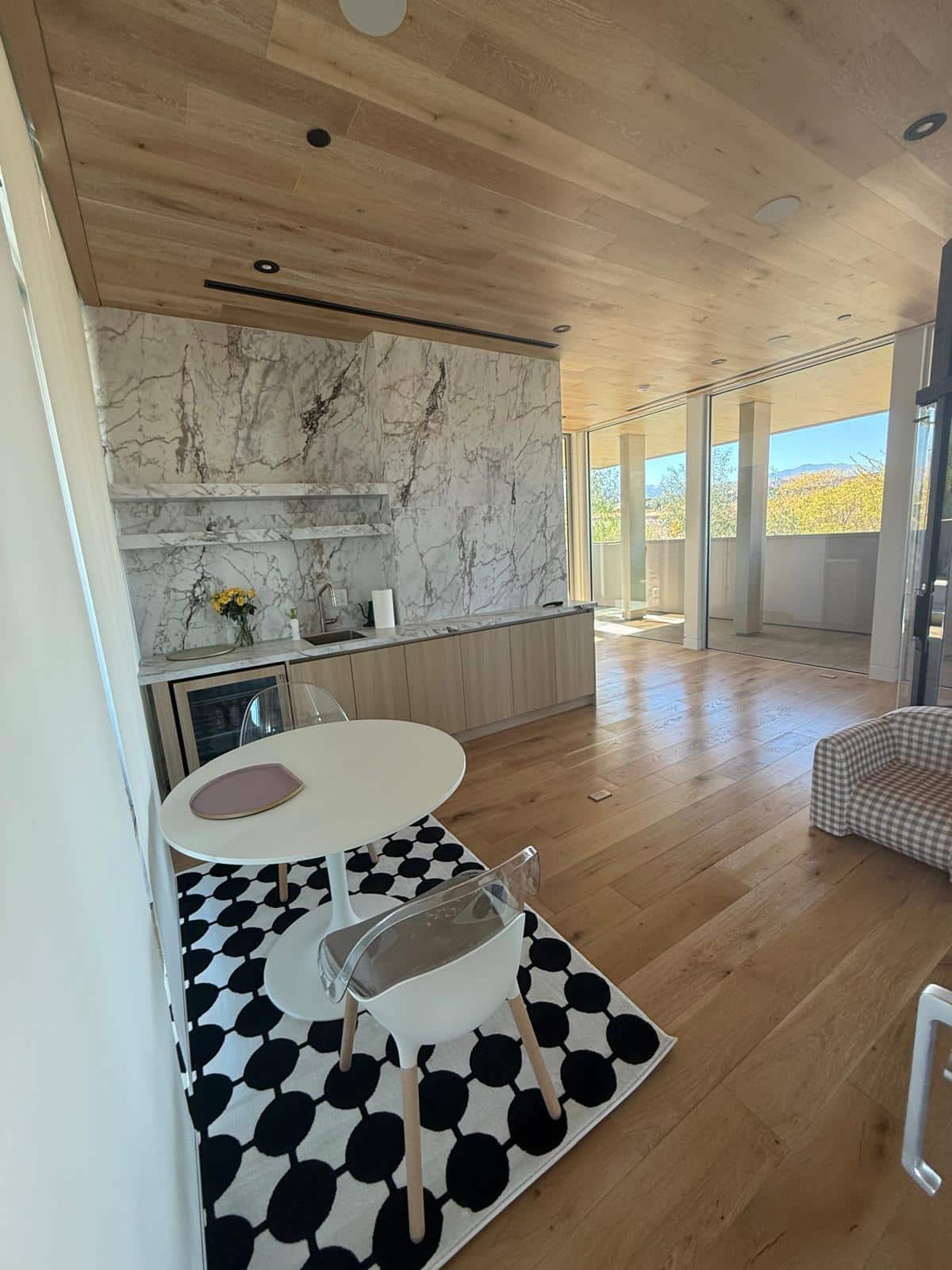 Open living and dining area with floor to ceiling veined stone look tile wall, wood plank ceiling and large windows