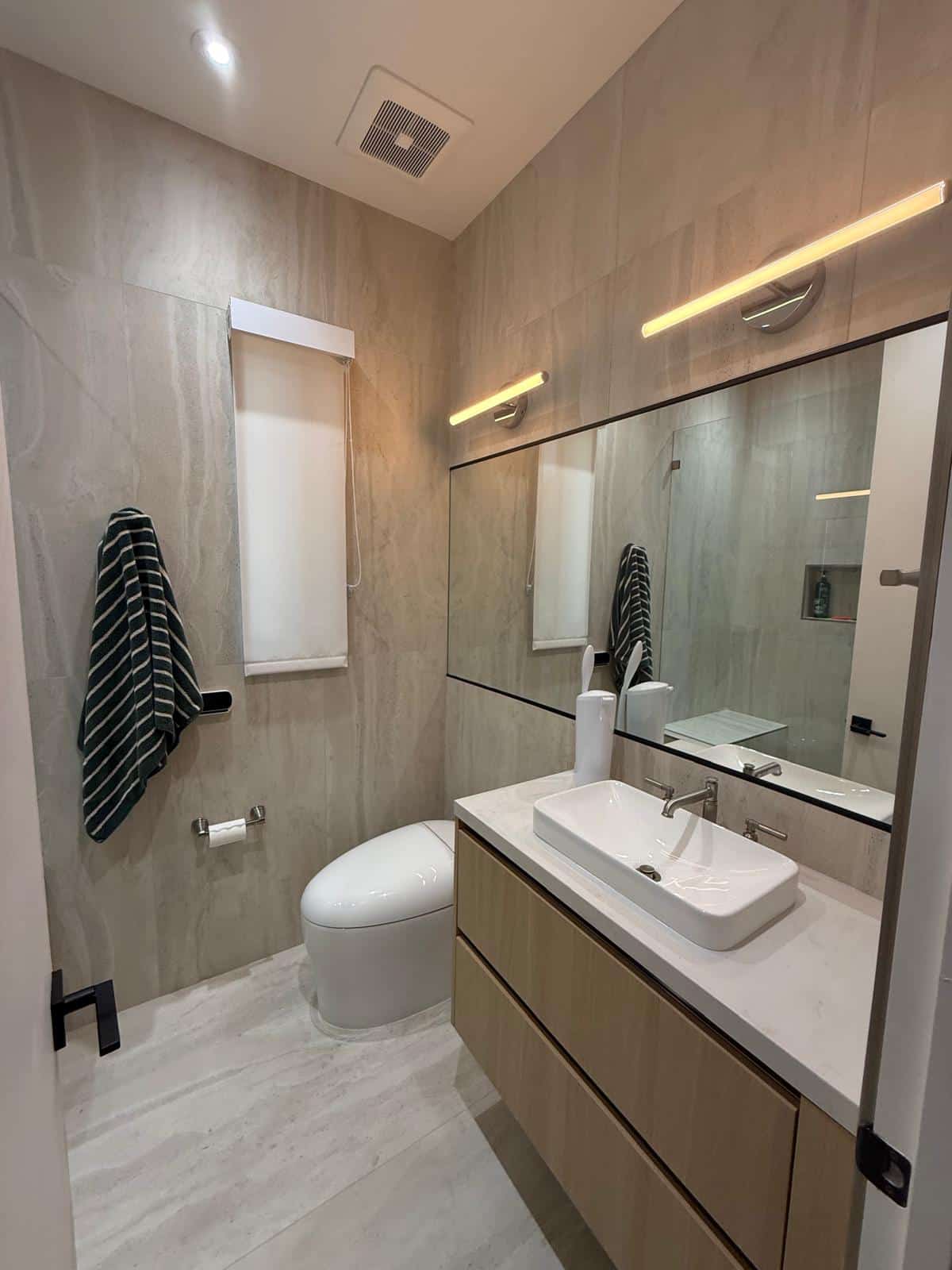Second bathroom with wood look wall tile, floating oak vanity, vessel sink, lit mirror and gray floor tile