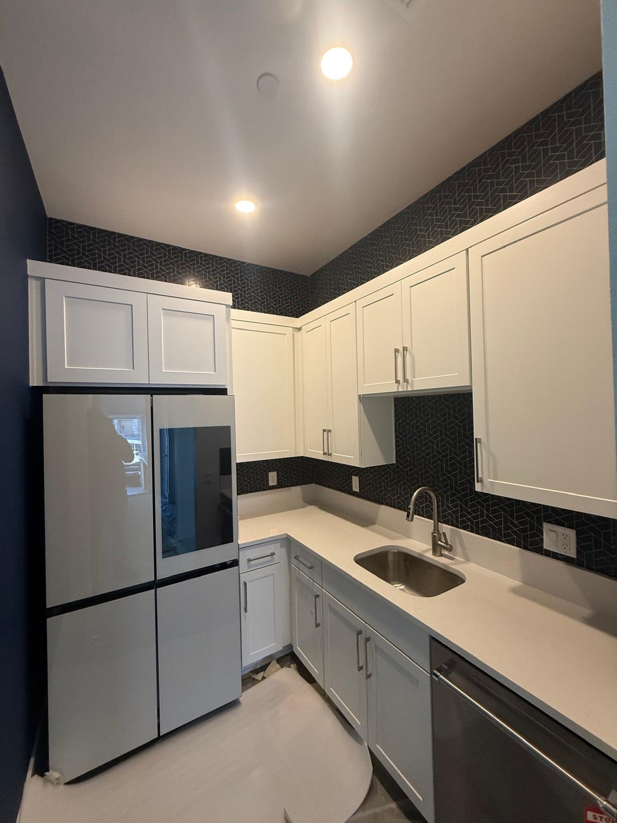 Kitchen with white shaker cabinets against dark backsplash tile and dark painted walls