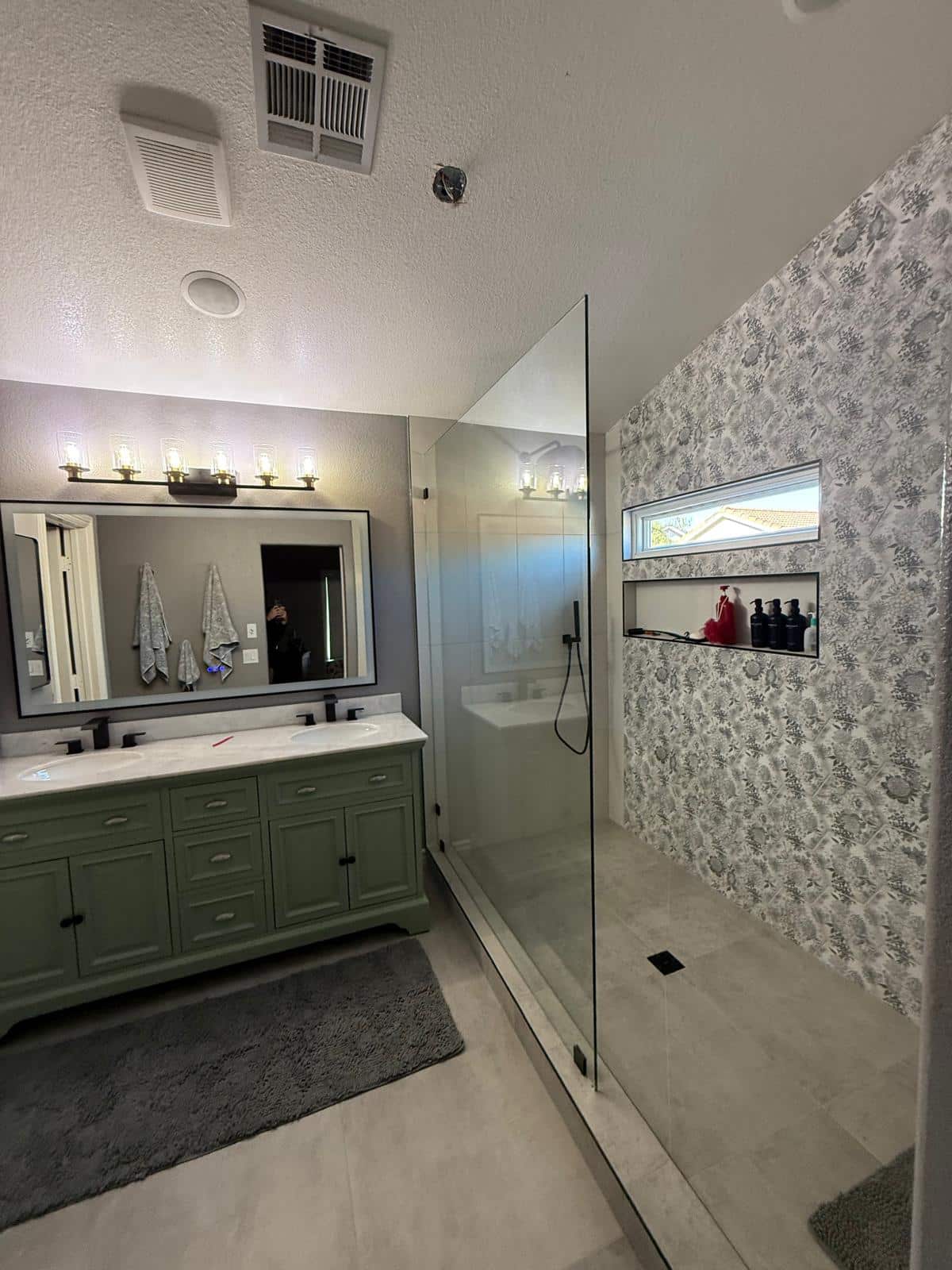 Remodeled bathroom with sage green vanity and walk-in shower with patterned tile