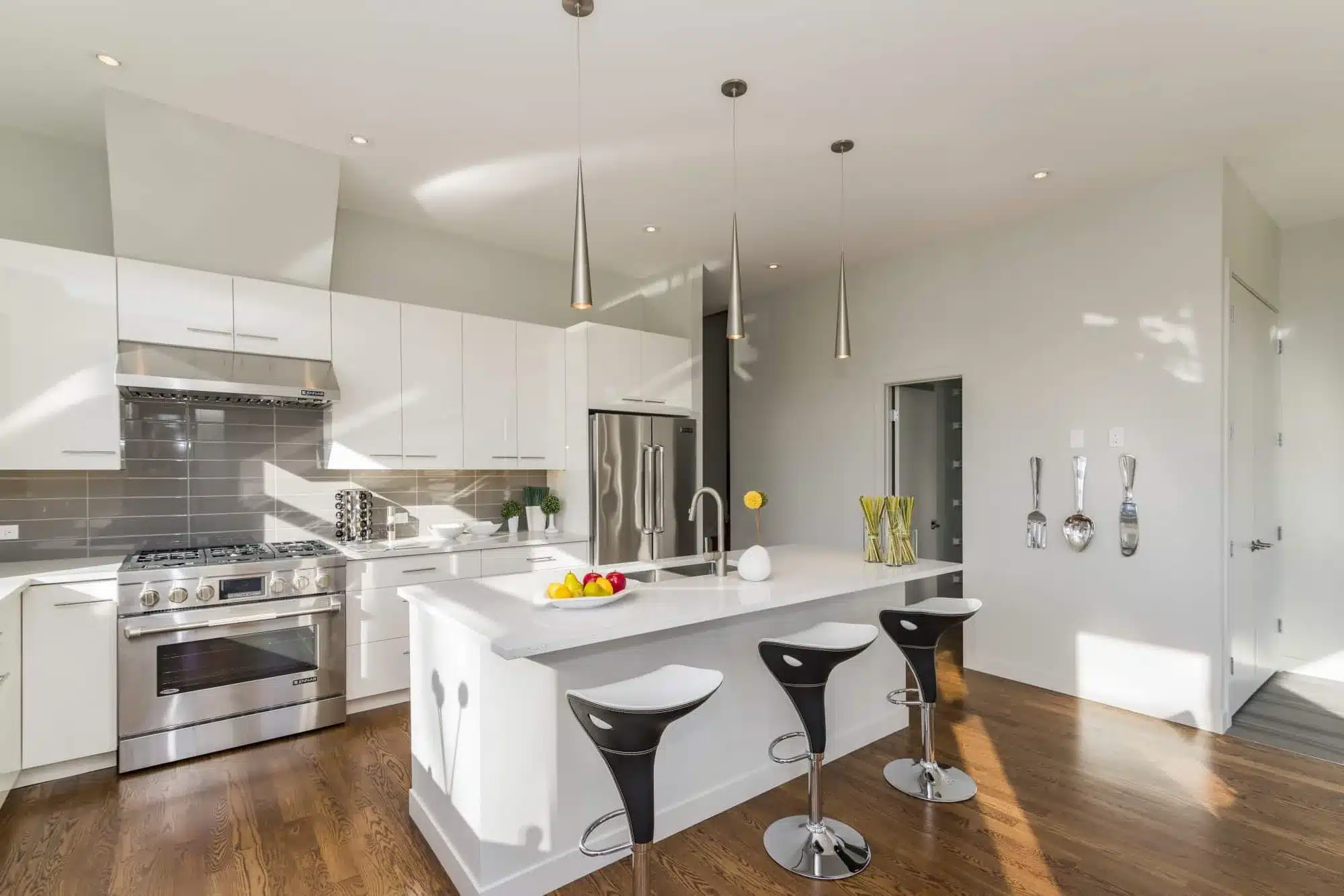 Modern kitchen with white cabinetry, stainless steel appliances, large white island with black stools, and pendant lighting