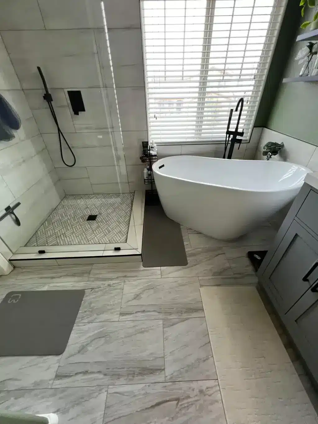 Contemporary bathroom with white freestanding tub, glass shower enclosure, and gray vanity under skylight