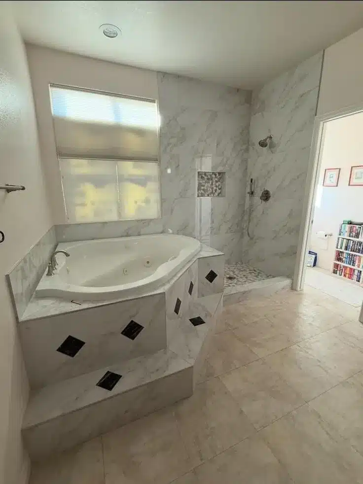 Corner jetted bathtub beside a shower with marble-look wall tile, a recessed niche, and a mosaic floor.