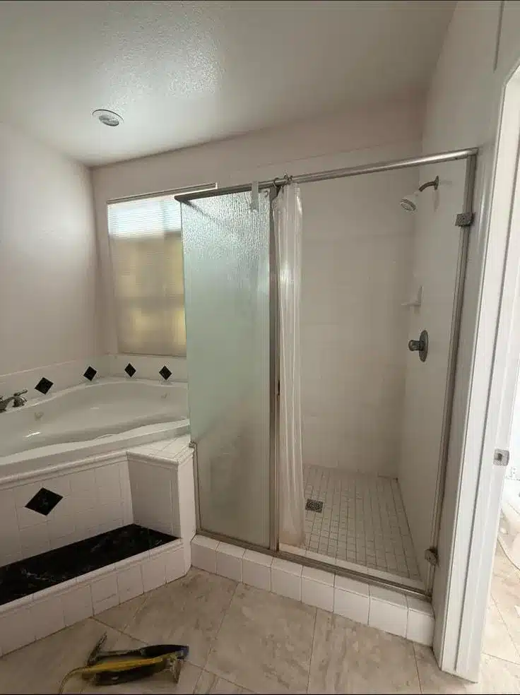 Tiled shower with a metal-framed textured glass panel beside a corner bathtub with black diamond tile accents.