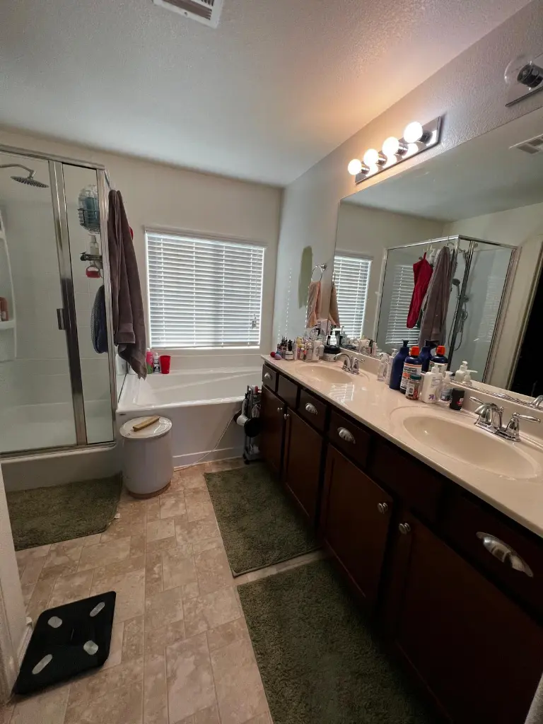 Bathroom with double-sink vanity, glass shower, soaking tub, and countertop toiletries beneath a large mirror.