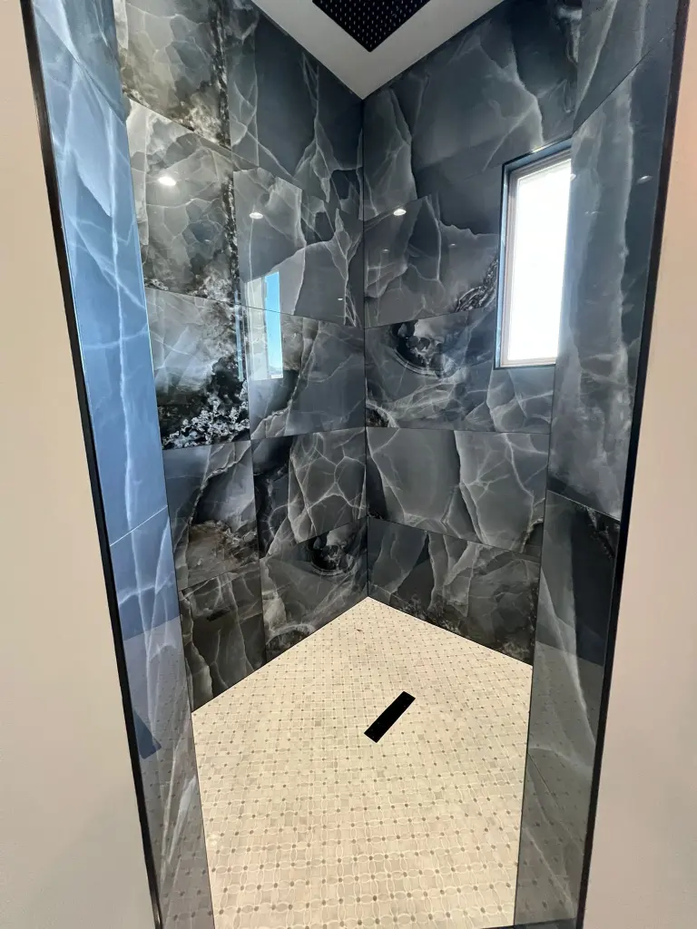 Walk-in shower with dark marble-look wall tiles, frameless glass, small window, and mosaic tile shower floor