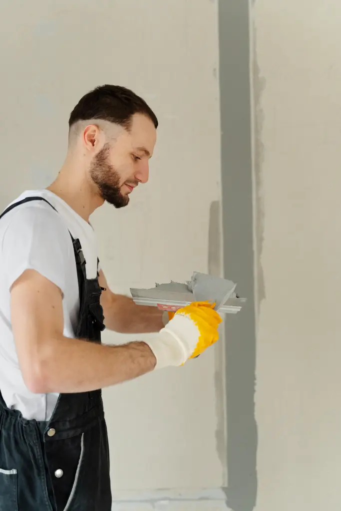 Tradesman applying drywall joint compound to a vertical wall seam using a taping knife