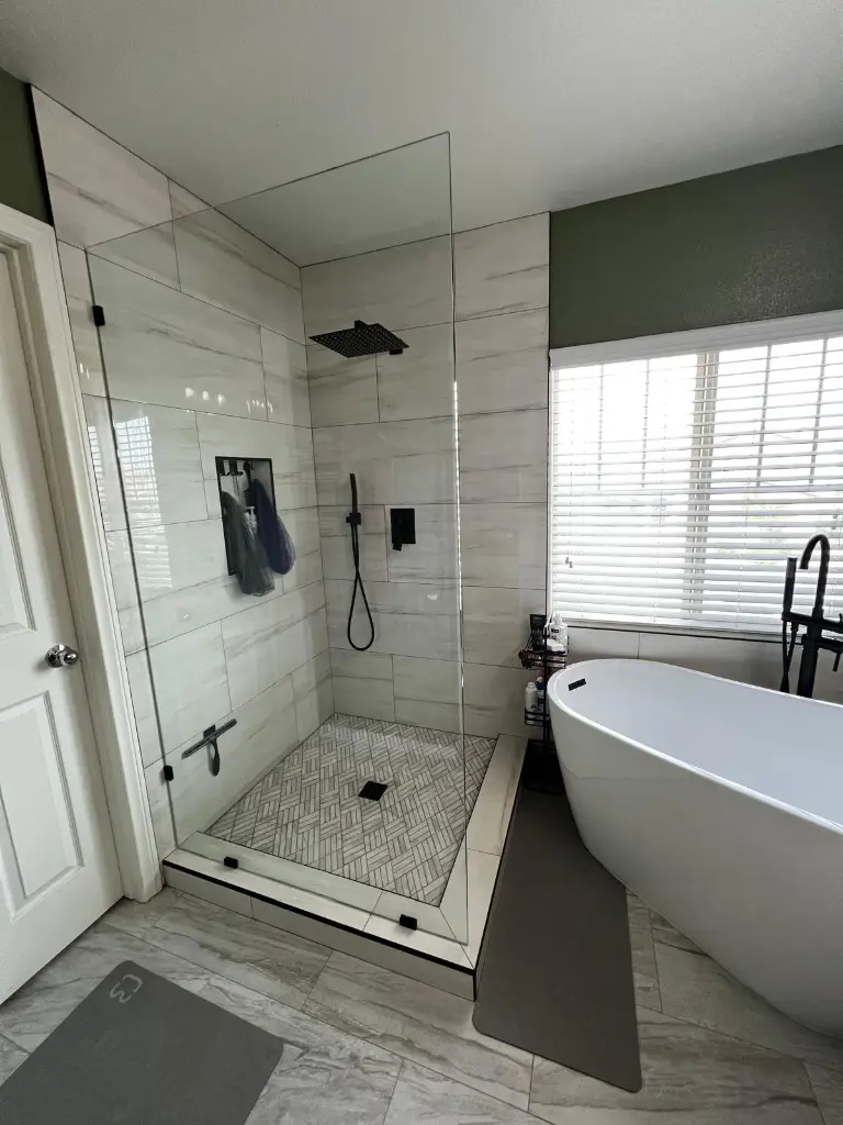 Walk-in glass shower beside a freestanding tub installed over heated bathroom floors with patterned tile in a modern bathroom