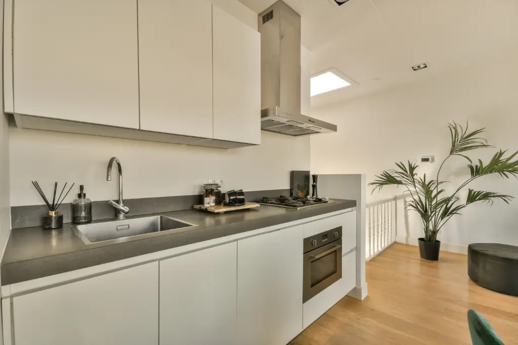 Minimalist galley kitchen with white cabinets, gray countertop, stainless range hood, and wood flooring