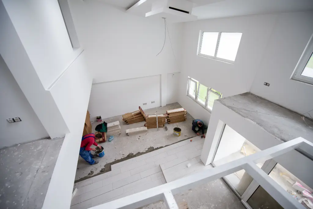 Modern home interior under construction with workers installing flooring in a double-height living space with large windows