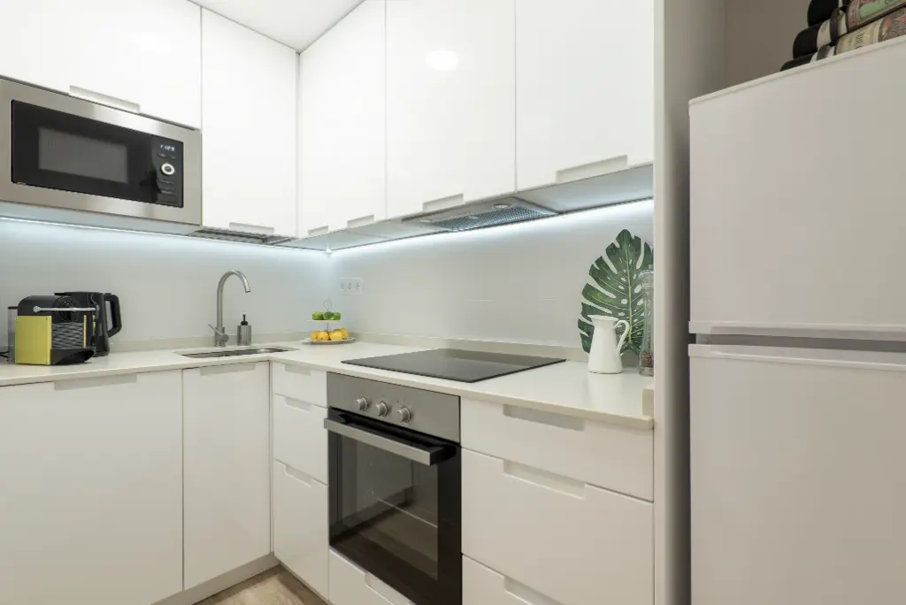 Modern white corner kitchen with built-in oven, microwave, induction cooktop, and under-cabinet lighting