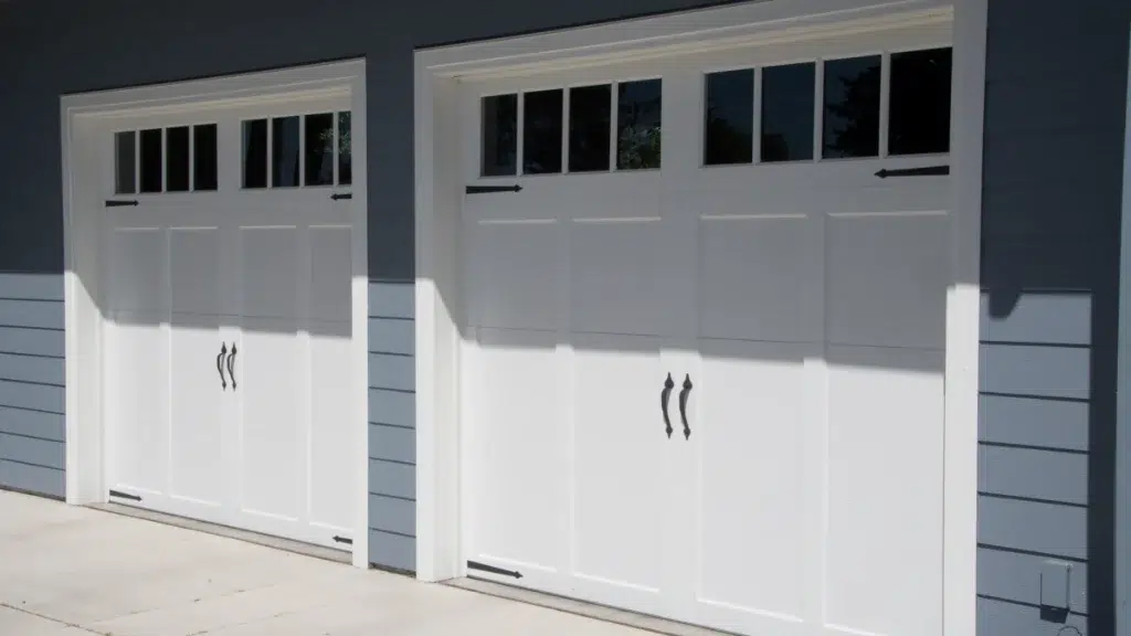 Two white carriage-style garage doors with upper windows on a blue-sided home.